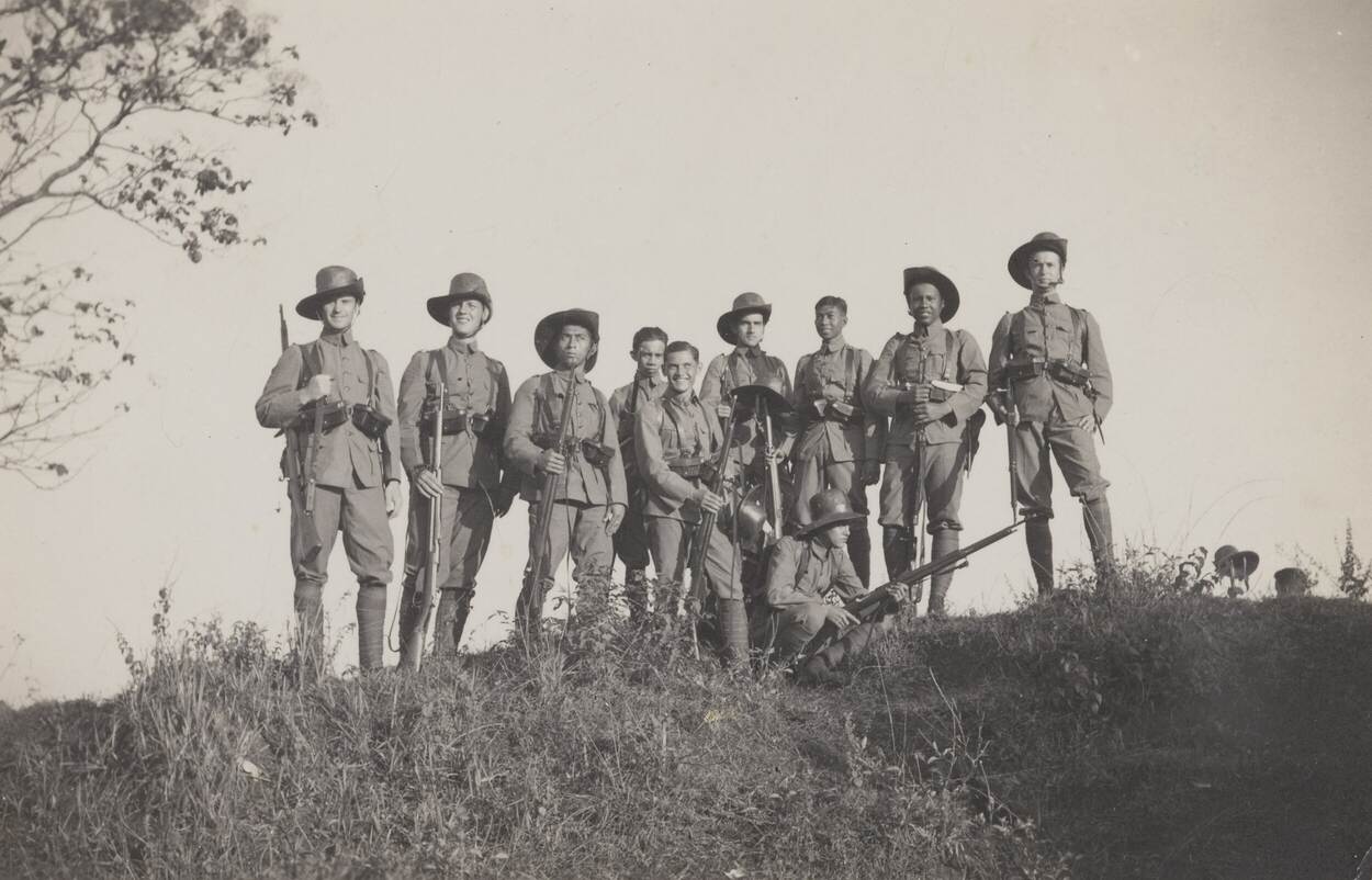 Zwart-witfoto van KNIL-militairen met bamboehoed en geweer in de hand.