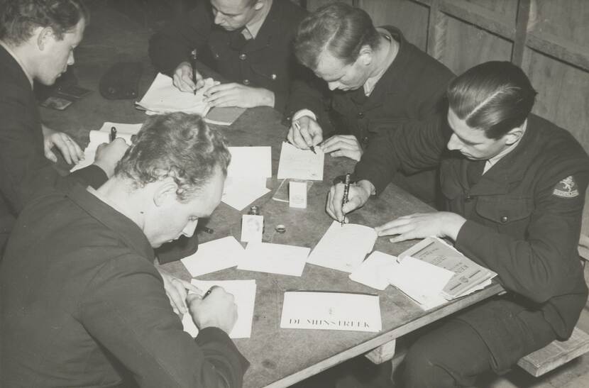 Zwart-witfoto, 5 mannen in militair uniform zitten aan een tafel voorovergebogen brieven te schrijven.