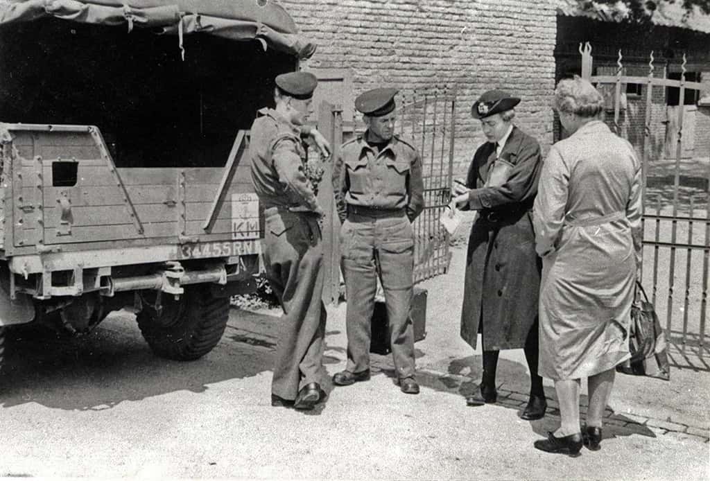 Zwart-witfoto, buiten. Er staan achter een vrachtwagen drie mensen aandachtig naar een vrouw te luisteren.