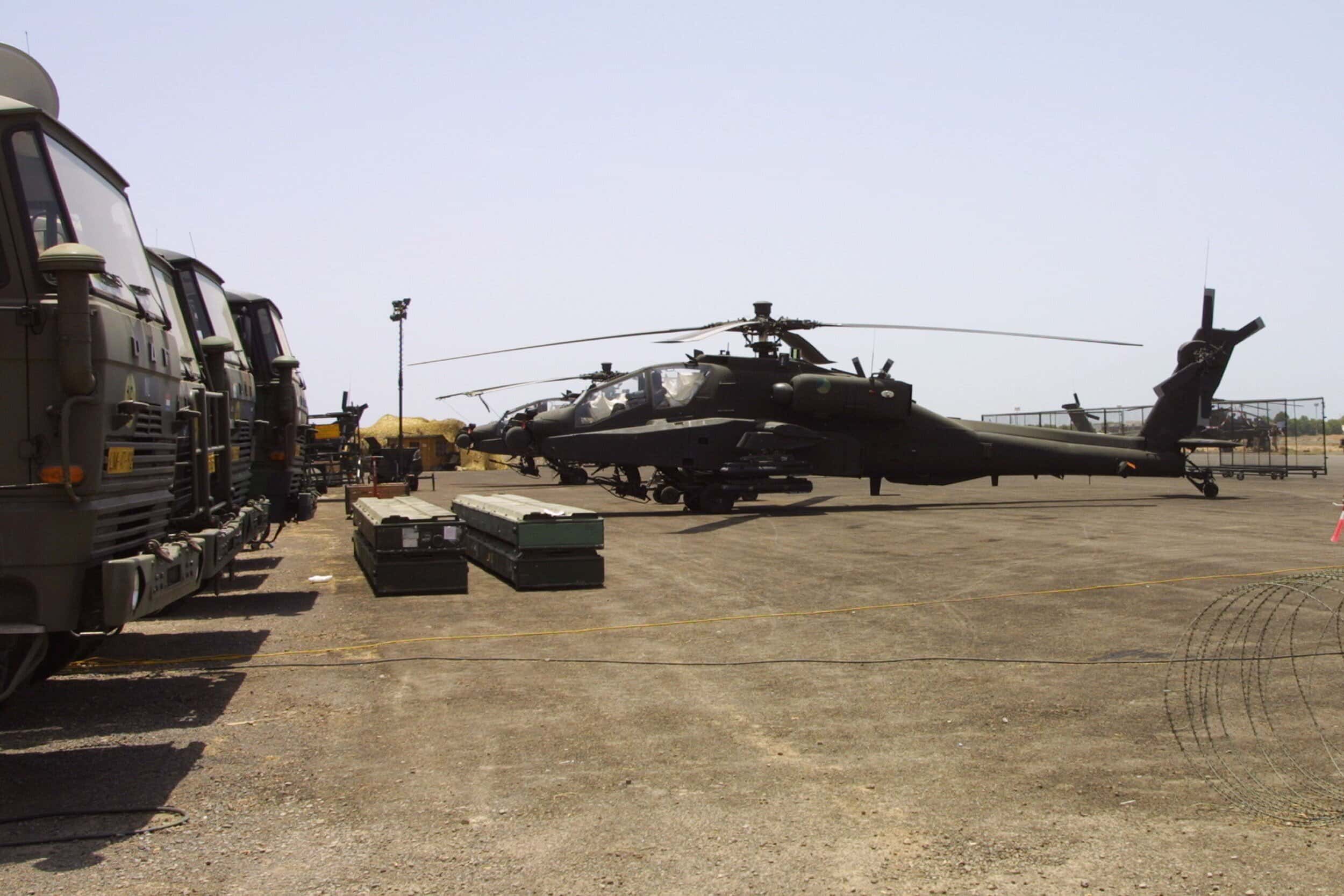 Kleurenfoto van een betonnen vlakte, links staan drie DAF-vrachtwagens geparkeerd, in het midden twee helikopters.
