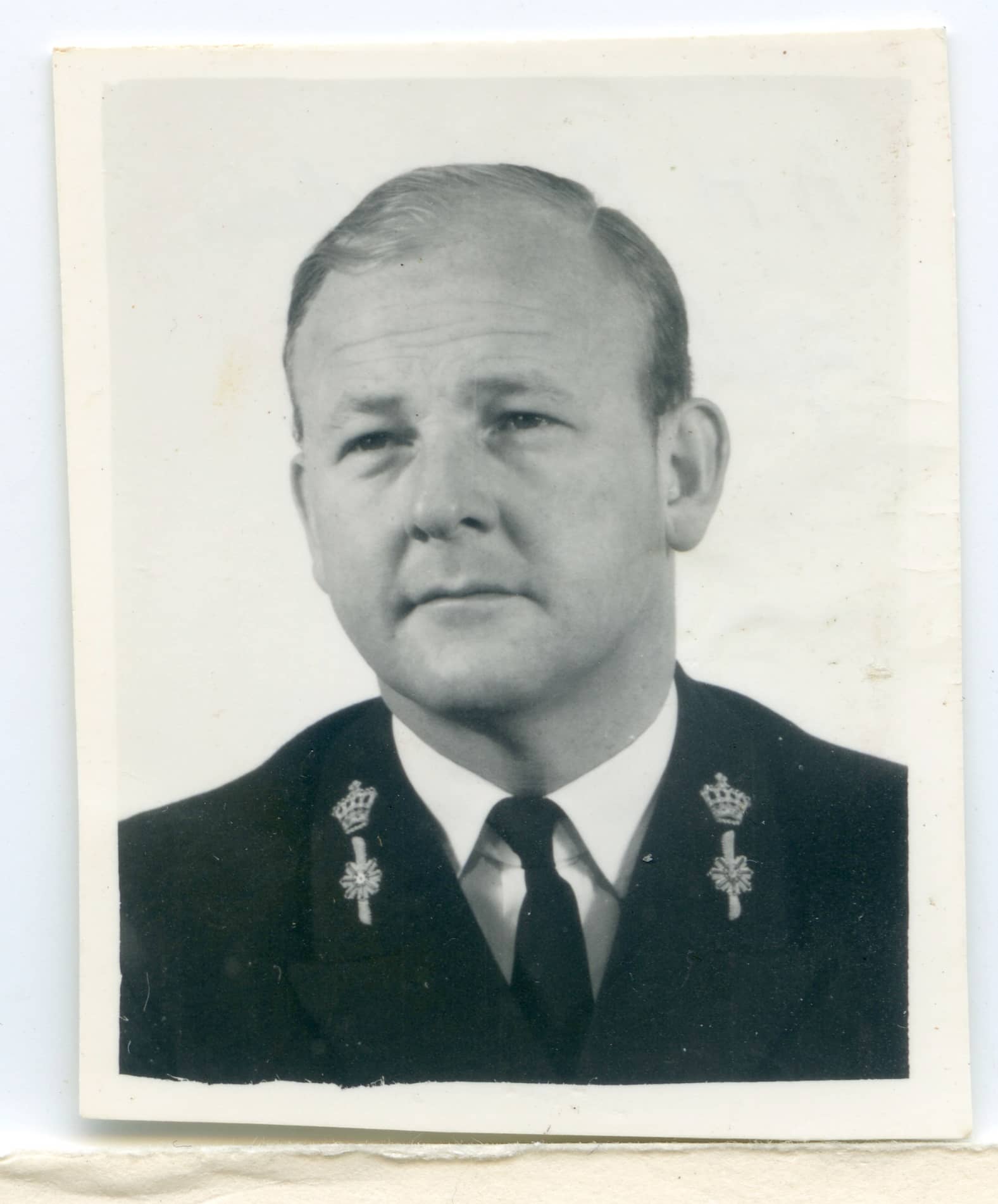 Zwart-witfoto. Dit is een portretfoto van een man. Het is nog net te zien dat hij een marine-uniformjas aanheeft, omdat op de boorden van zijn jas een kroon en daaronder het roer van een schip staat. Onder de jas zit een wit overhemd met een zwarte stropdas. De man zelf kijkt schuin langs de camera. Hij heeft kort blond haar, dat netjes in een scheiding is gekamd.