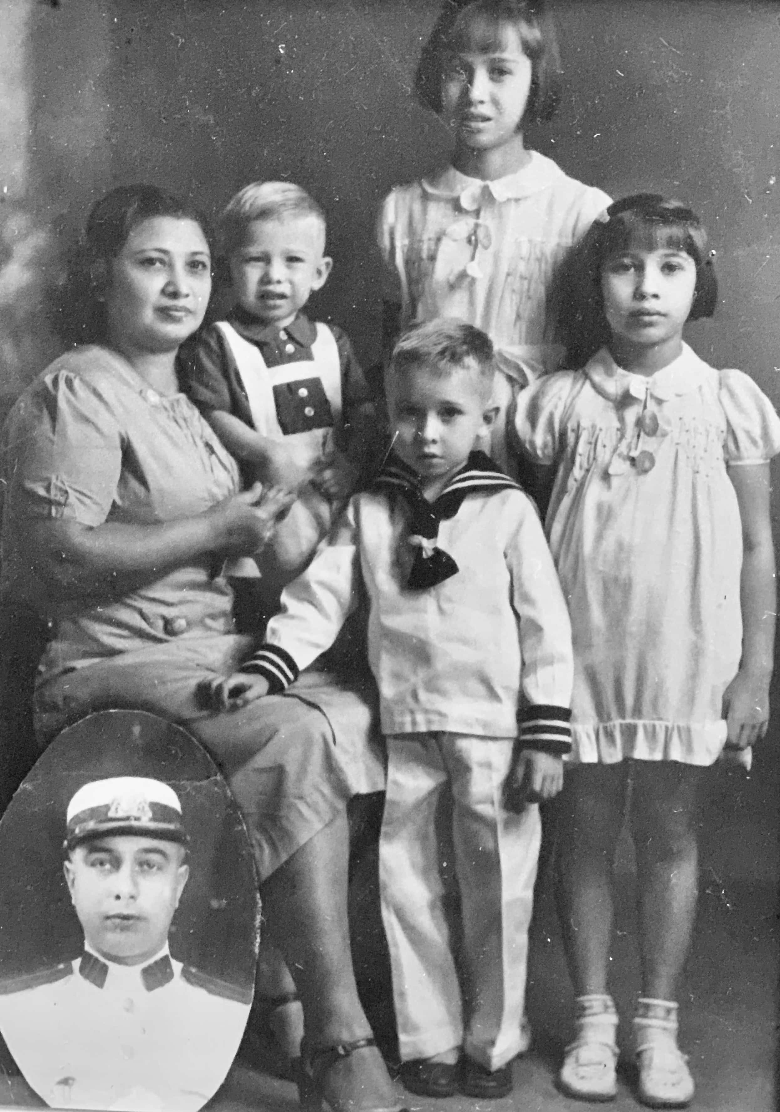Zwart-witfoto. Groepsfoto van een vrouw en vier kinderen. De vrouw zit links en heeft een jongetje op de arm. Vooraan staat een ander jongetje in een wit matrozenpakje. Achteraan en rechts staan twee meisjes in nette jurkjes. Links onderin is in een ovaal het portret van een man in wit uniform bijgeplakt.