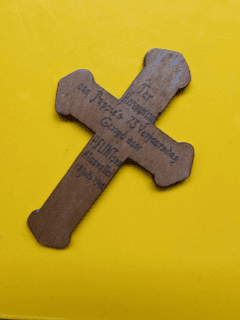 Kleurenfoto. Een bruin kruis van hout op een gele achtergrond. Op het kruis staat geschreven: ter herinnering aan Pappie’s 73 verjaardag gewijd door P. Flint Alasvallei 18 juli 1941.