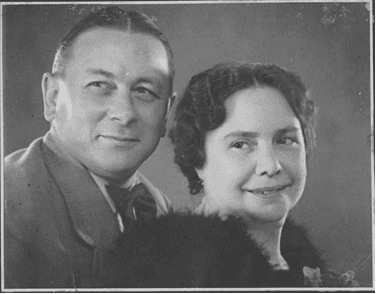 Zwart-witfoto. Portretfoto van een man en een vrouw. De man is links, hij draagt een donkerkleurig pak met strik, zijn haar zit netjes schuin naar achteren gekamd met een scheiding in het midden. De vrouw is rechts, zij draagt iets van bont om haar schouders, haar haar is donker krullend. Ze kijken allebei vanuit de ooghoeken naar iets links buiten beeld.