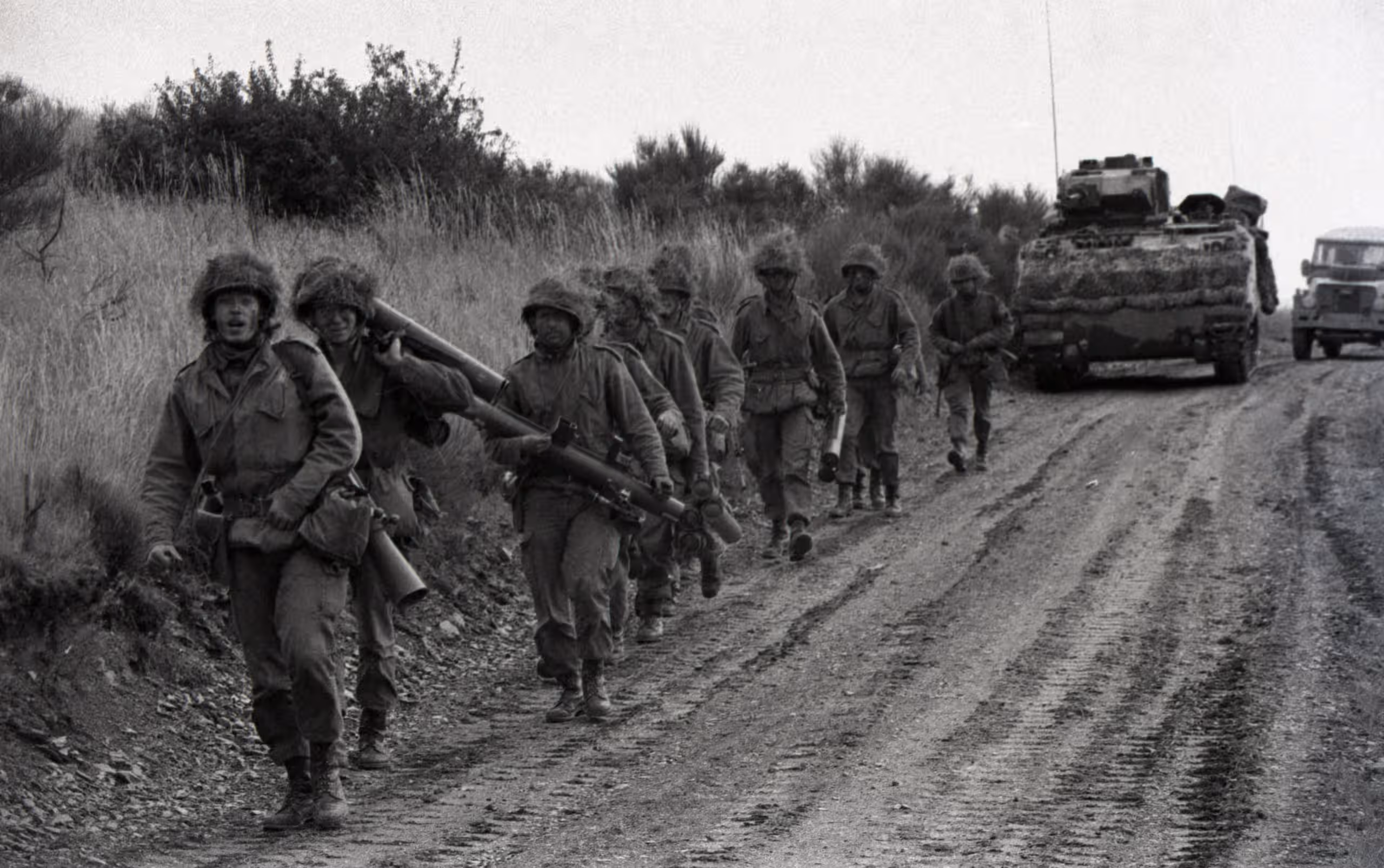 Zwart-wit foto. Een groep militairen in uniform marcheert buiten.