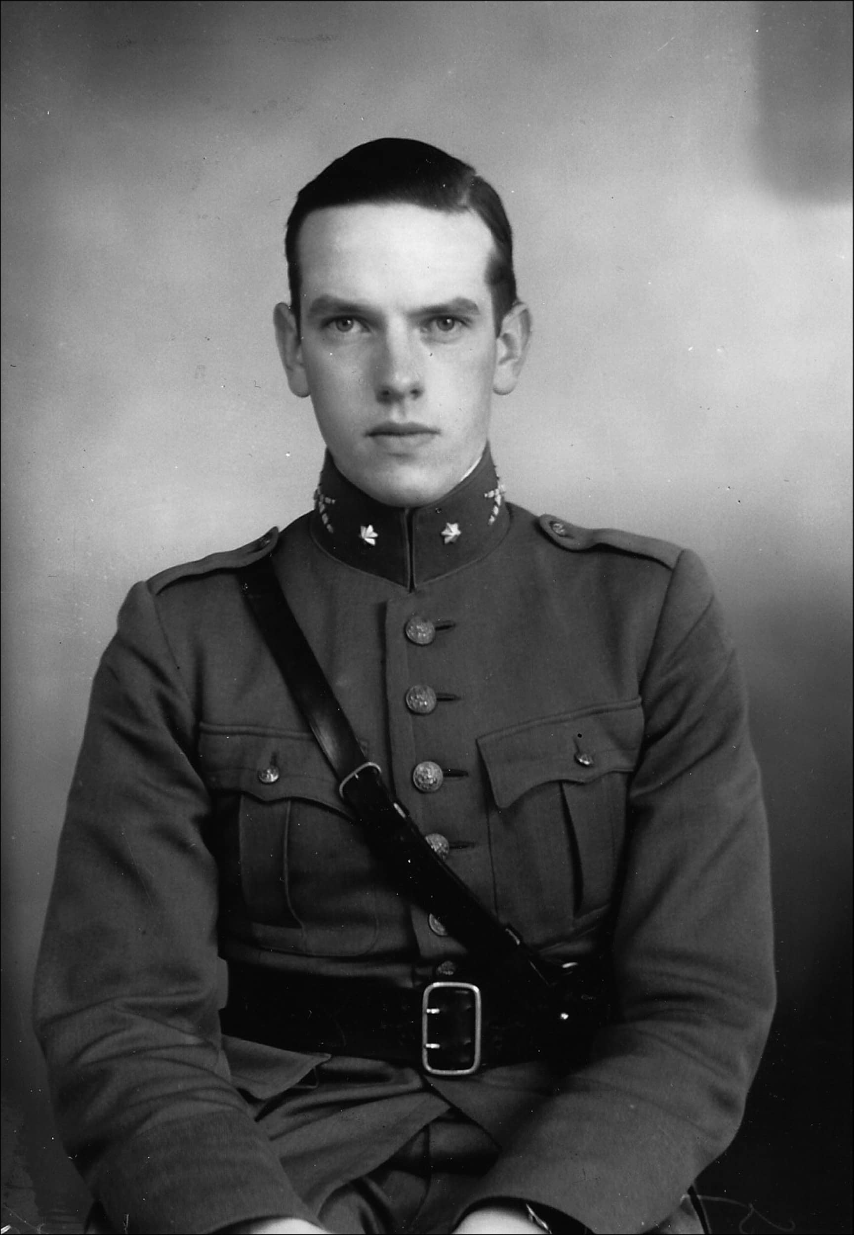 Zwart-witfoto. Jonge man in uniform kijkt recht de camera in.