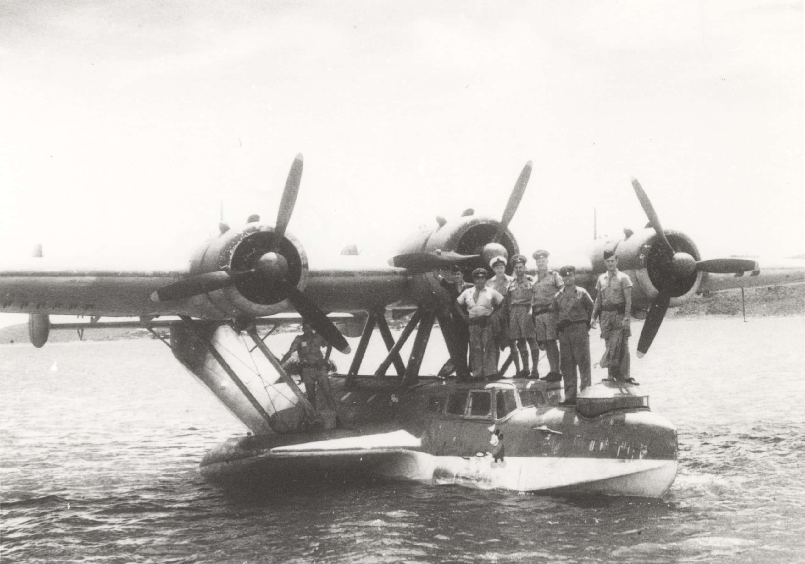 Zwart-witfoto. Een aantal mannen staat op de voorkant van een vliegboot.