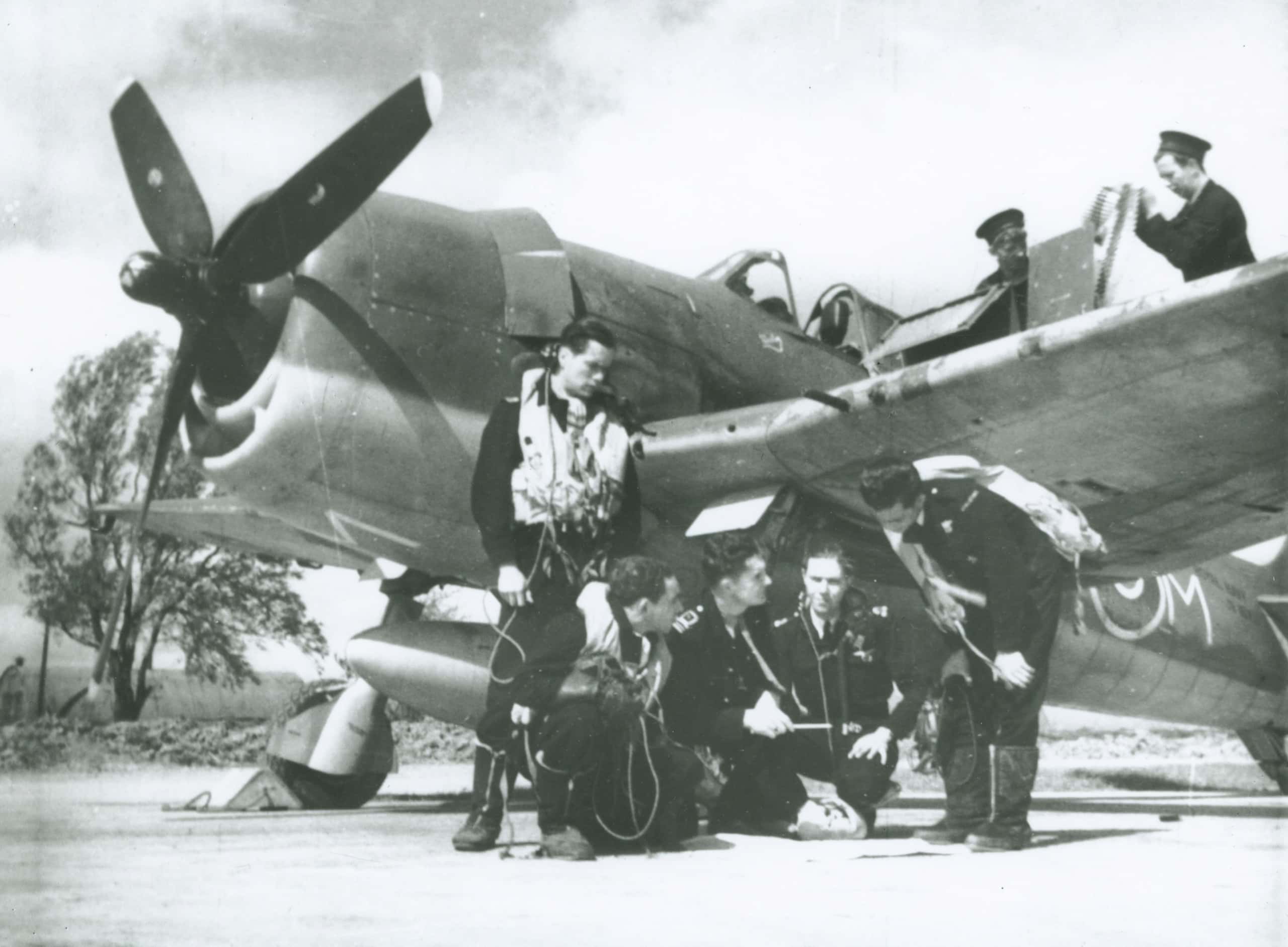 Zwart-witfoto. Een groepje mannen staat voor een vliegtuig.