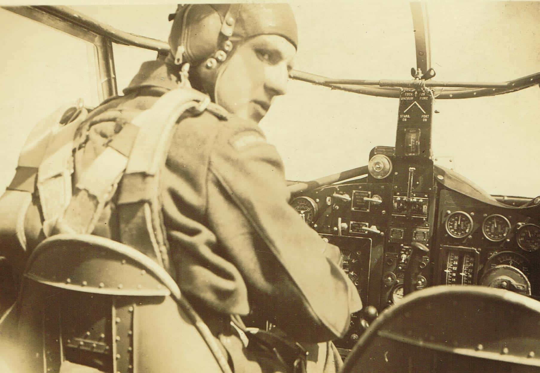 Zwart-witfoto van man in militair vliegeruniform in een cockpit van een vliegtuig.