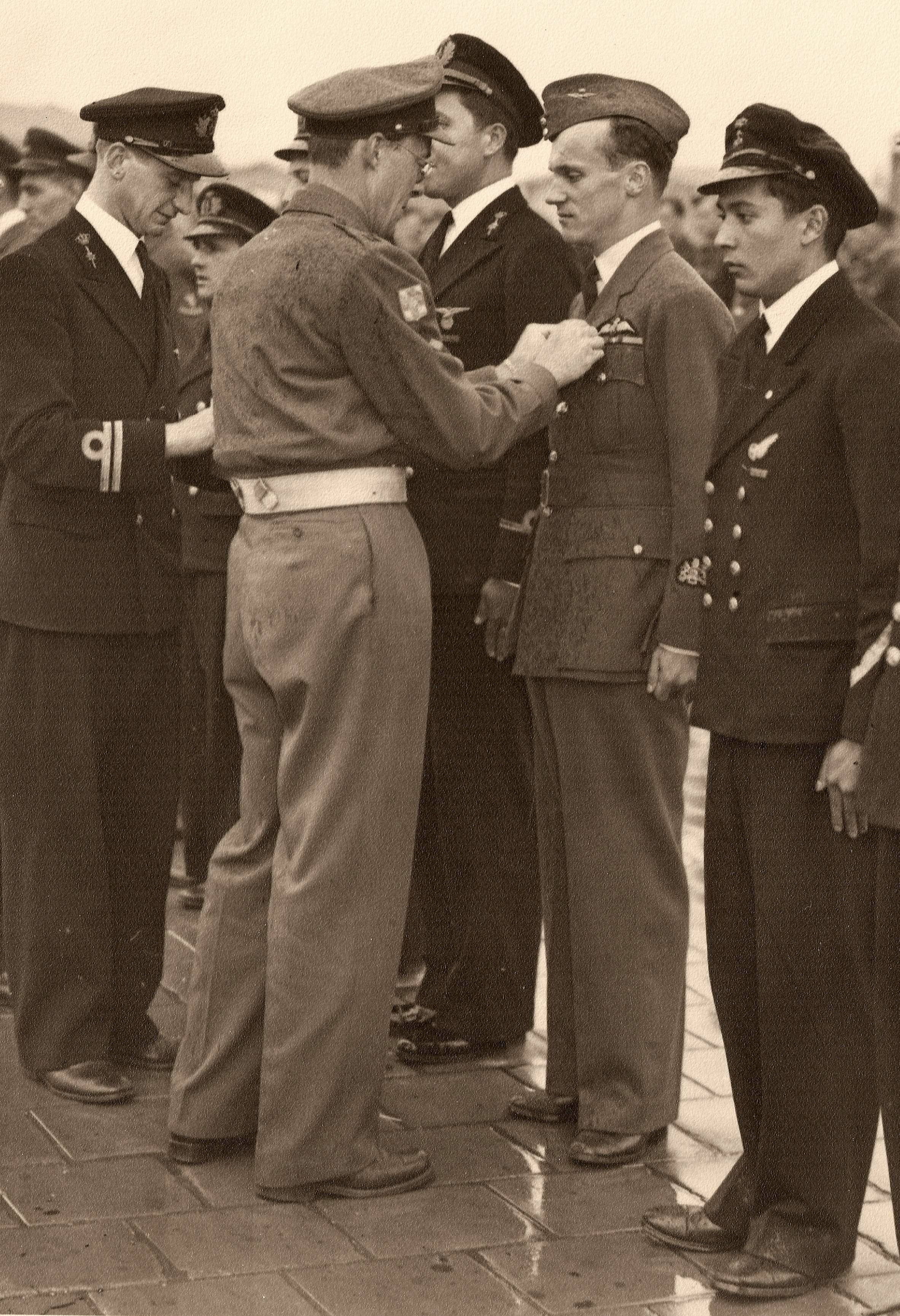 Zwart-witfoto. Mannen in militair uniform. Een man speldt een onderscheiding bij een andere man op de borst.