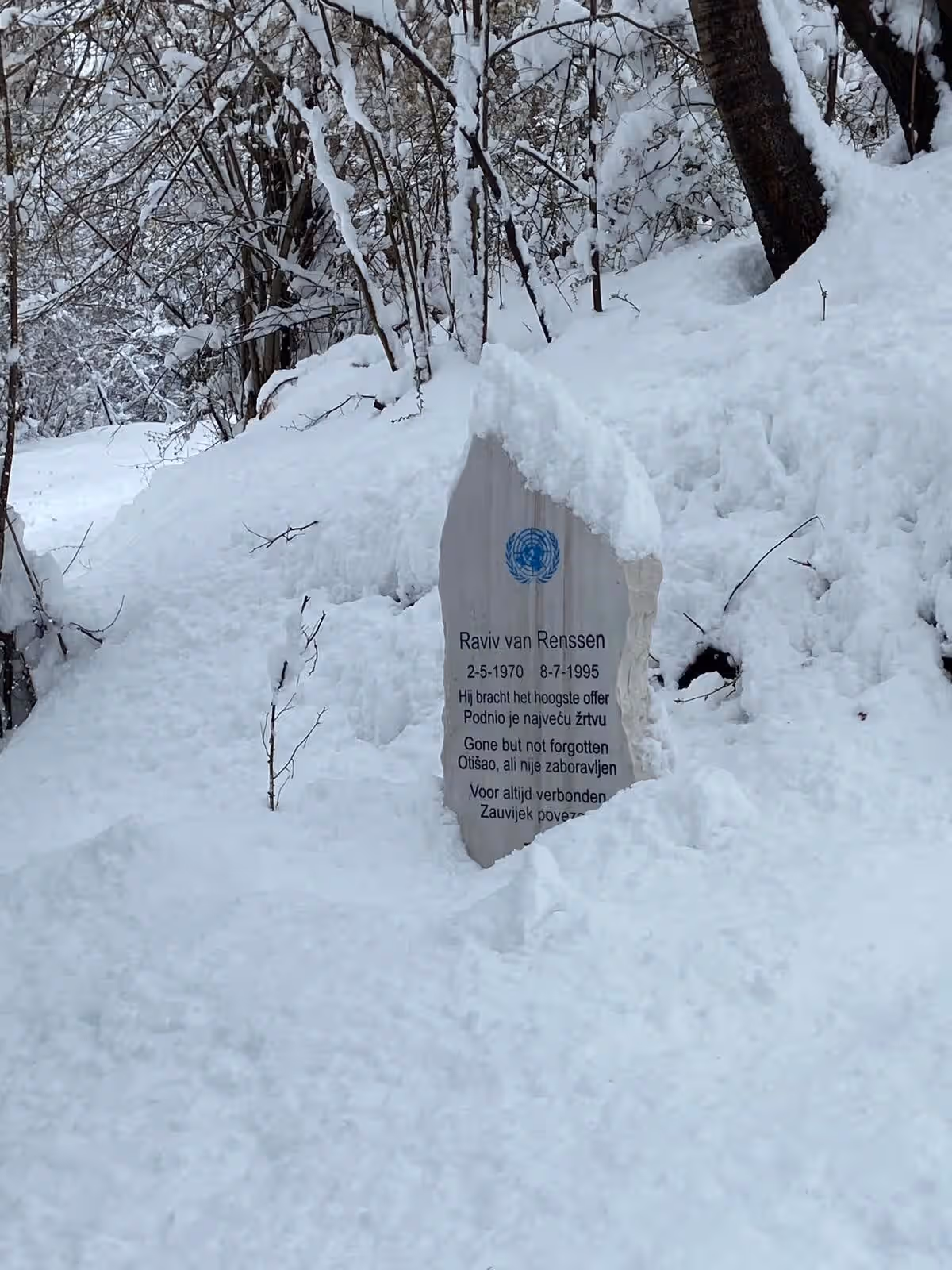 Kleurenfoto. In de sneeuw is een grafsteen te zien.