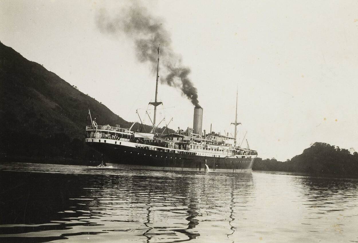 Zwart-witfoto van het koopvaardijschip Van Imhoff varend langs de kust. Uit de schoorsteen van het stoomschip komt zwarte rook.