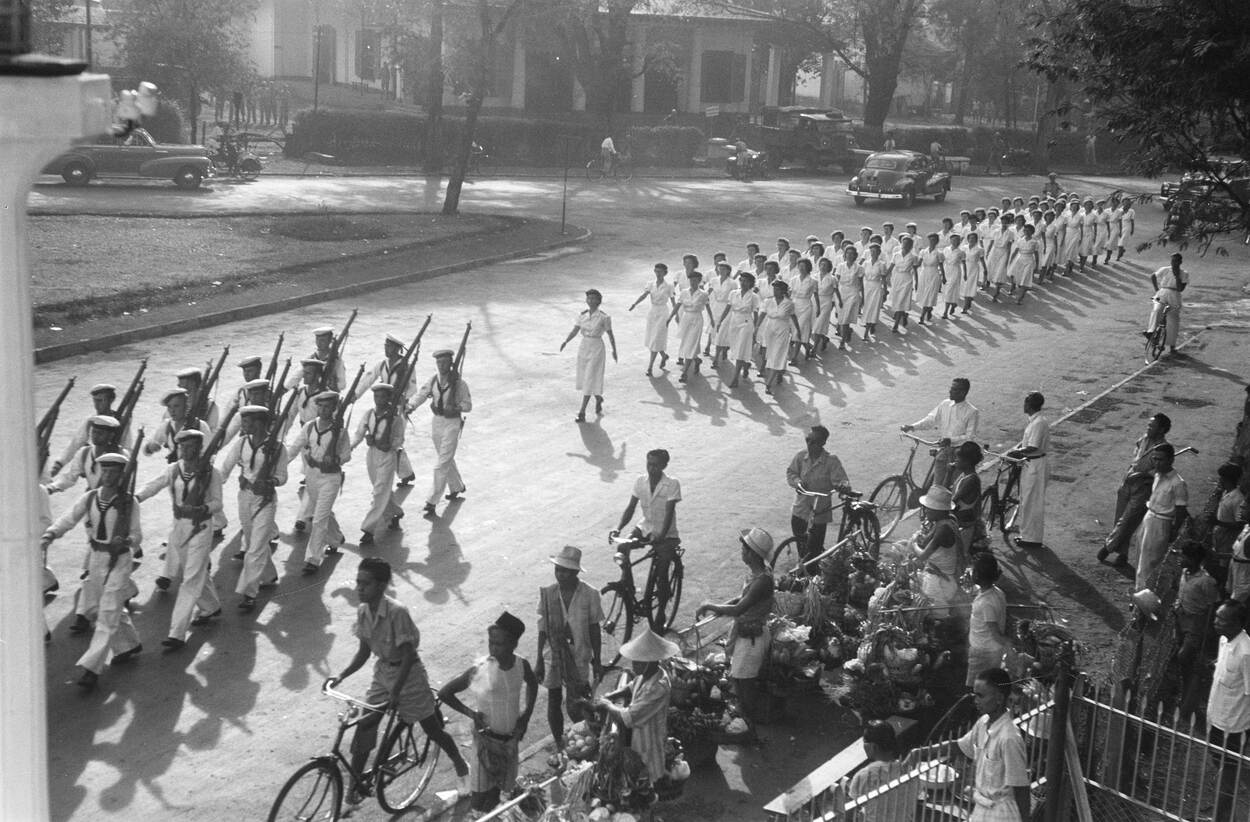 Zwart-witfoto van een detachement marva's paraderend door een Indonesische straat.