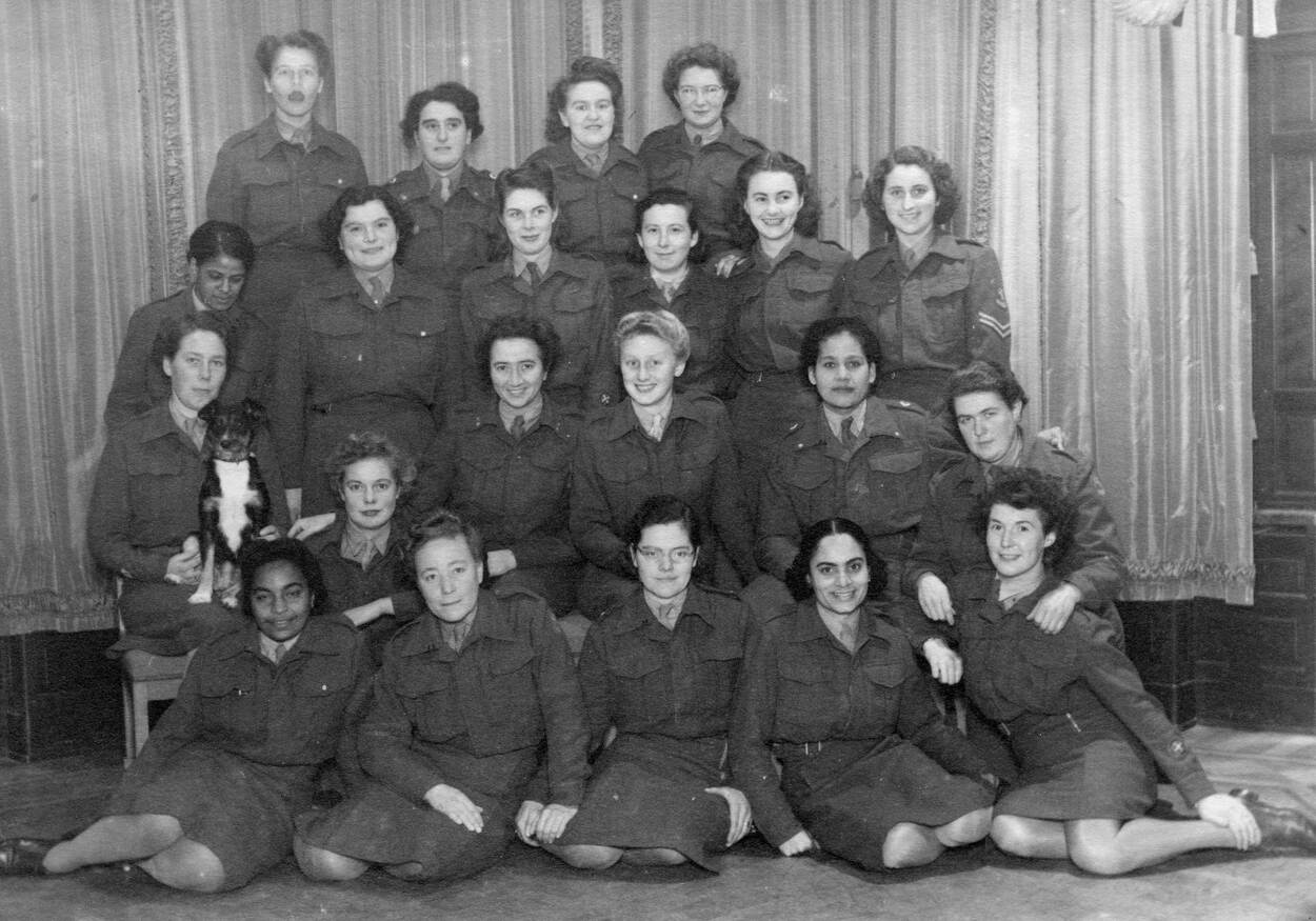 Zwart-witportretfoto van 22 vrouwen in militair uniform, 1 van hen heeft een hond op schoot.