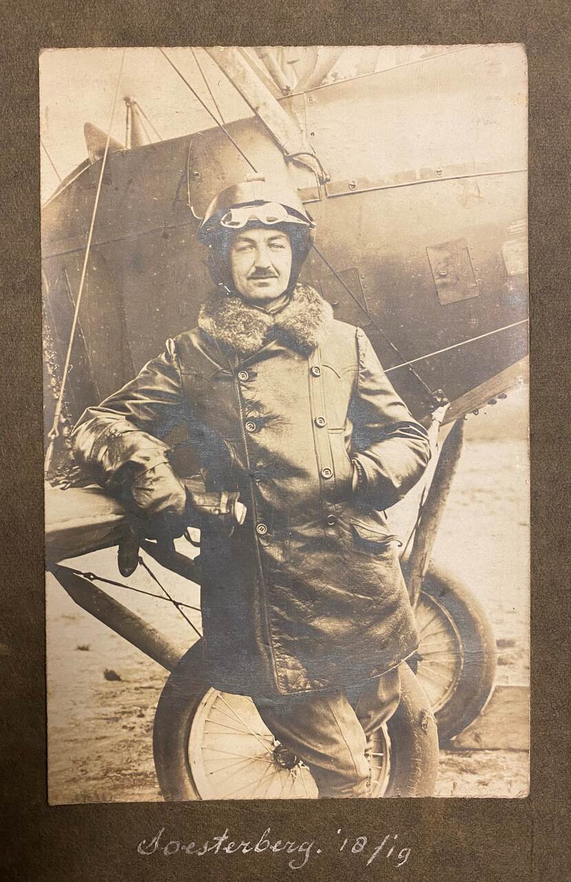 Vlieger-waarnemer Jan Koopman poseert voor een vliegtuig op vliegbasis Soesterberg. Het betreft een zwart-wit foto. Koopman draagt een leren jas, met een bontkraag.