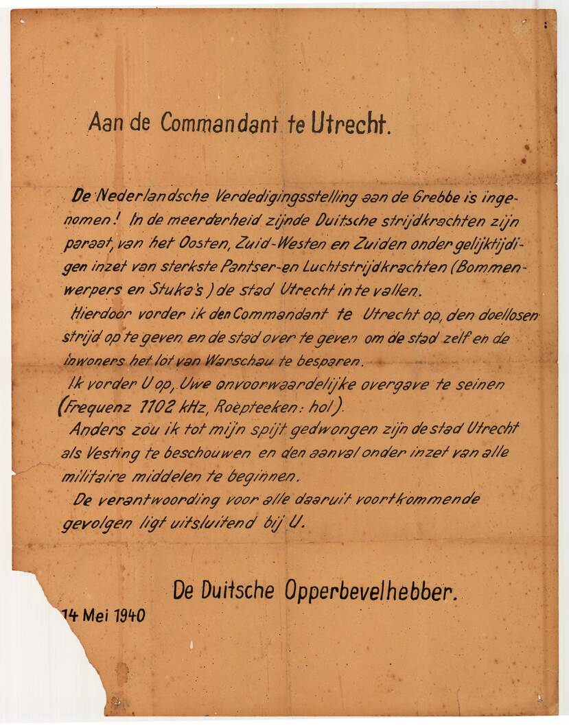 Kleurenfoto. Vergeeld papier met een tekst, aanhef is “Aan de commandant te Utrecht”. In de tekst wordt een ultimatum gegeven omtrent de overgave van de stad, getekend “De Duitsche Opperbevelhebber” en de datum 14 mei 1940. De linker benedenhoek van het papier ontbreekt.