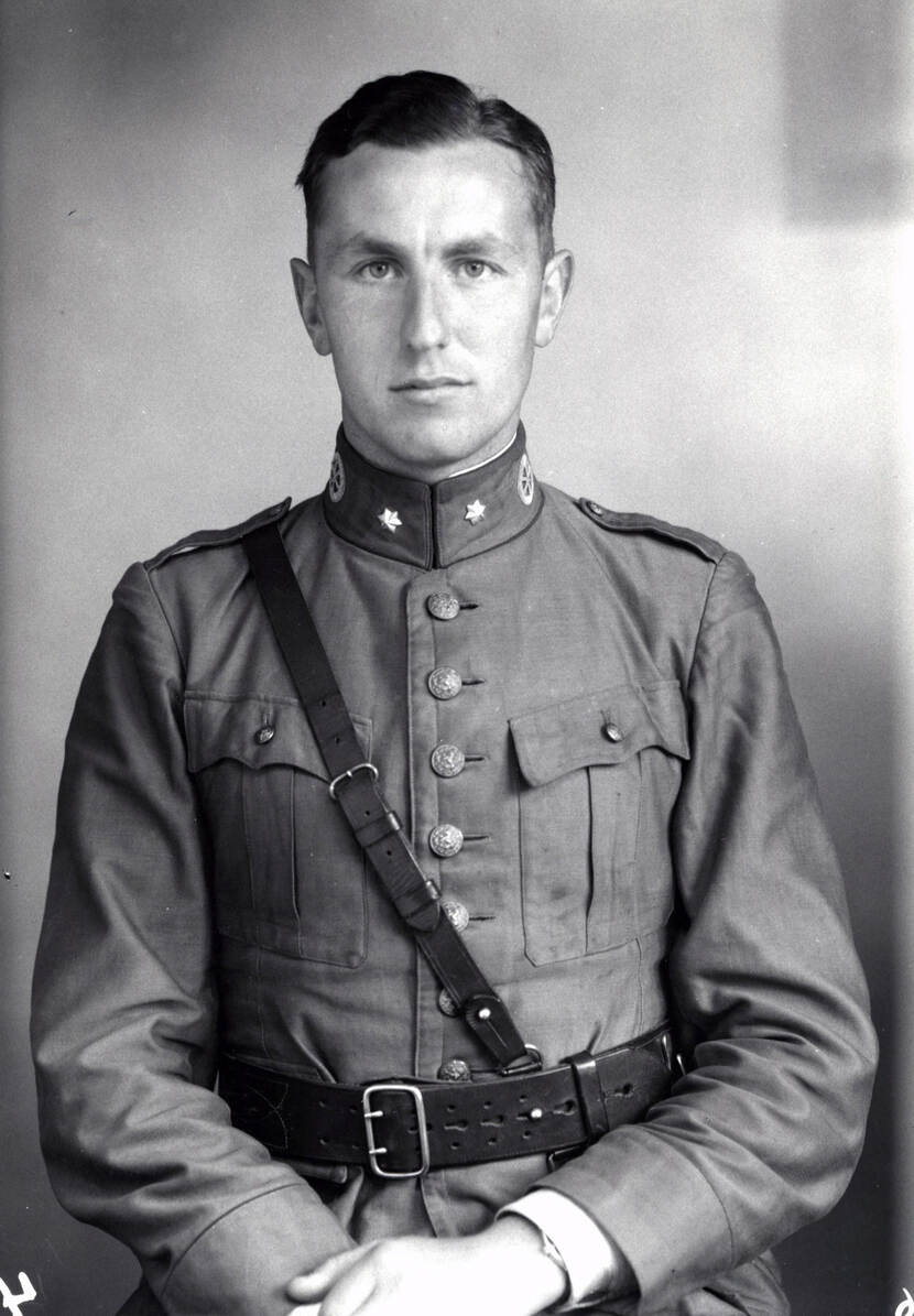 Zwart-witfoto. Portret van een militair. Hij draagt een uniform, met zeven grote knopen over de borst, een brede leren riem om zijn middel en een smallere leren riem schuin over de borst. Op zijn kraag is aan weerszijden een zeshoekige ster aangebracht.