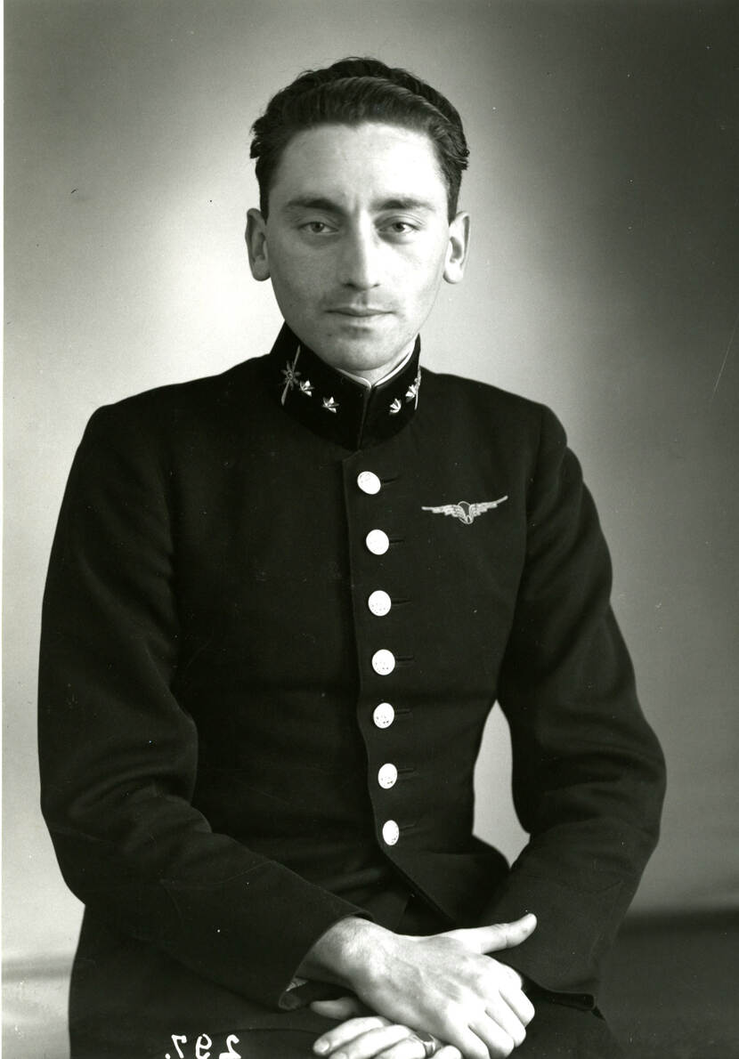 Zwart-witfoto. Portret van een ongeschoren militair, hij kijkt recht in de camera. Hij draagt een donker uniform met zeven grote knopen over de borst, zijn handen op elkaar gevouwen op zijn schoot, op de linkerborst een embleem van een W met vleugels. Op zijn kraag zijn aan weerszijden twee zeshoekige sterren aangebracht.