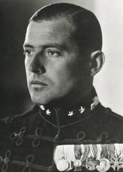 Zwart-witfoto. Portret van een militair, hij kijkt naar links buiten de camera. Hij draagt een donker uniformjas met touwtjes als versiersels, aan de kraag zijn aan weerszijden twee zeshoekige sterren aangebracht, op de borst draagt hij een rij van zes medailles.