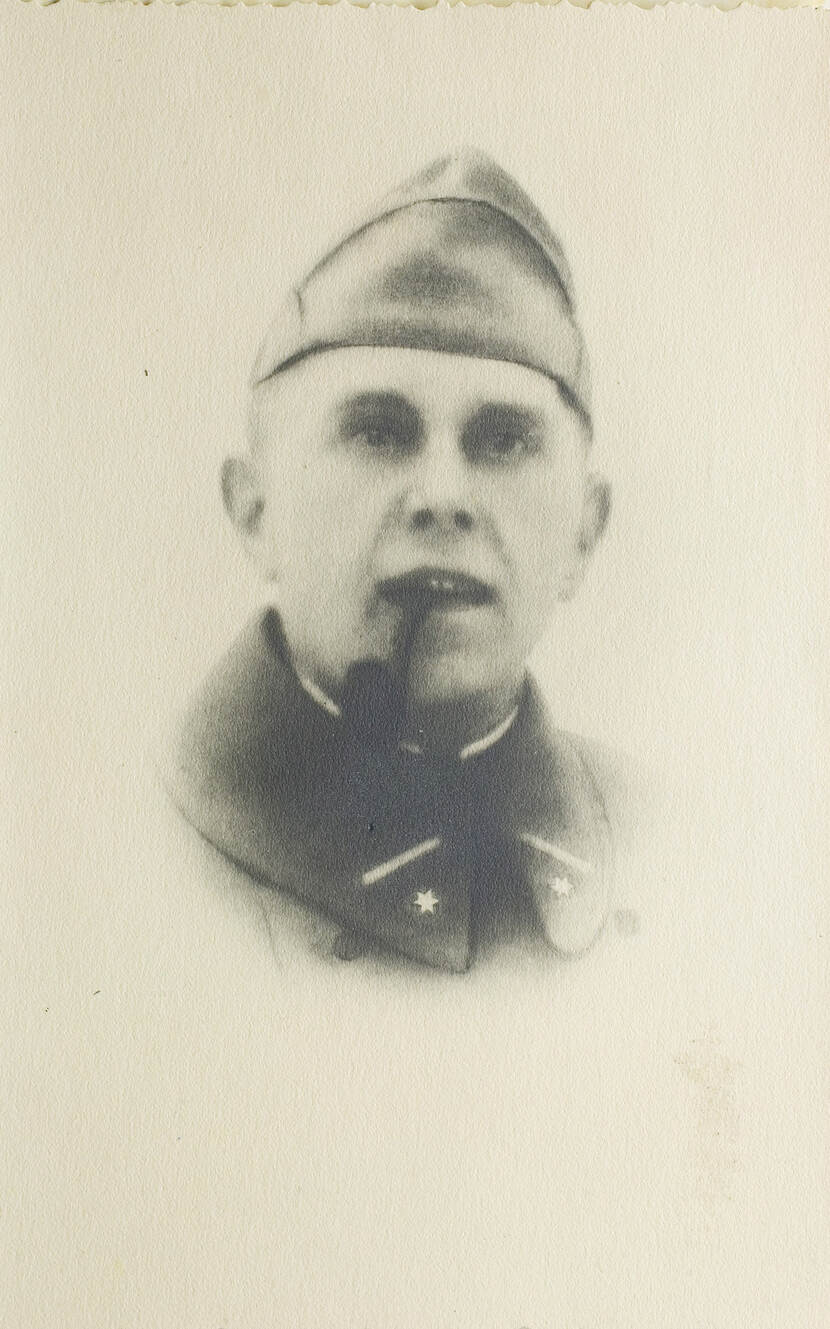Zwart-witfoto. Portret van een militair, alleen zijn hoofd is te zien. Hij draagt een dikke jas en een muts, op de kraag van zijn jas zijn aan weerszijden een zeshoekige ster aangebracht. Zijn mond hangt halfopen, waar hij een pijp in houdt.