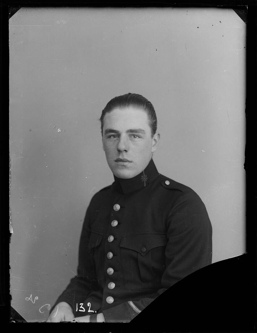 Zwart-witfoto. Portretfoto van een militair, hij zit naar links gedraaid en kijkt recht in de camera. Hij draagt een donker uniform met zeven grote knopen aan de voorkant, zijn handen op zijn schoot, zijn har is strak naar achteren gekamd.
