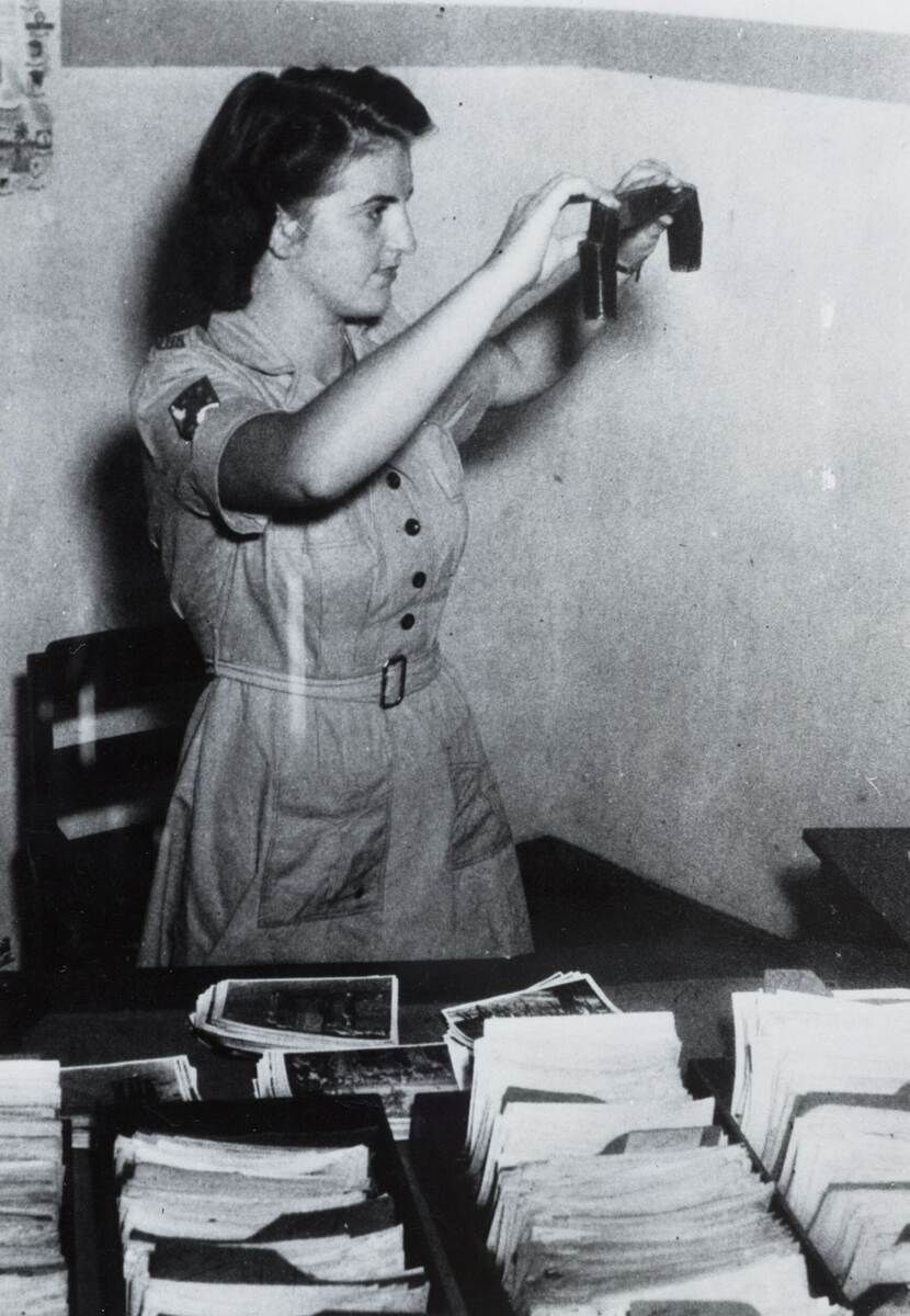 Zwart-witfoto, een vrouw in militair uniform houdt een negatiefstrook tegen het licht.