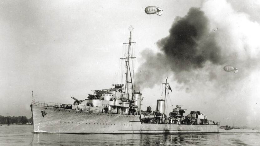 Torpedobootjager Hr.Ms. Isaac Sweers in het water. Enorme rookpluimen komen van het schip af vanwege de voortstuwing. In de lucht zijn twee ballonnen te zien.