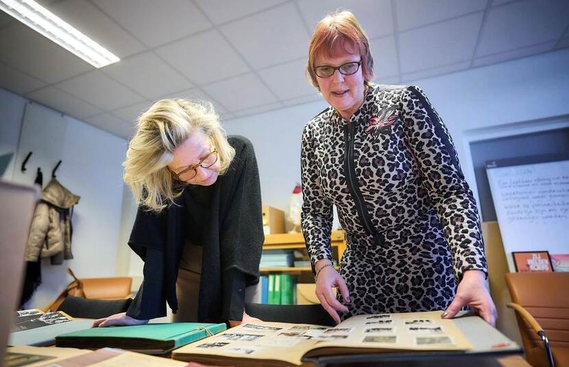 Foto in kleur met links in het zwart gekleed de minister van defensie. Rechts op de foto staat Nicolette Faber-Wittenberg. Samen bekijken zij oude foto's in een werkkamer.